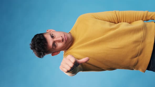 Unsatisfied man looking at camera and showing thumb down while standing on an blue background