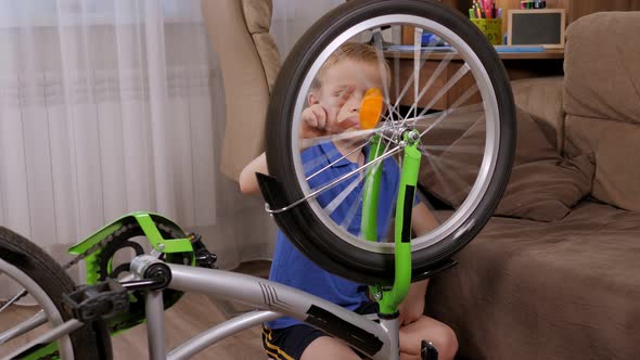 A Little Boy is Sitting on the Floor Next to a Bicycle He is Spinning a Wheel