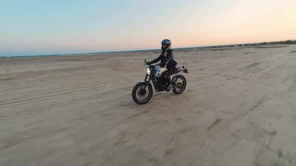 Young Stylish Woman Motorcyclist Driving Her Motorcycle in the Desert Road During Sunset