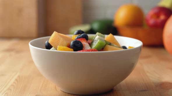 Camera follows putting mint leaves into a fruit salad bowl. Slow Motion.