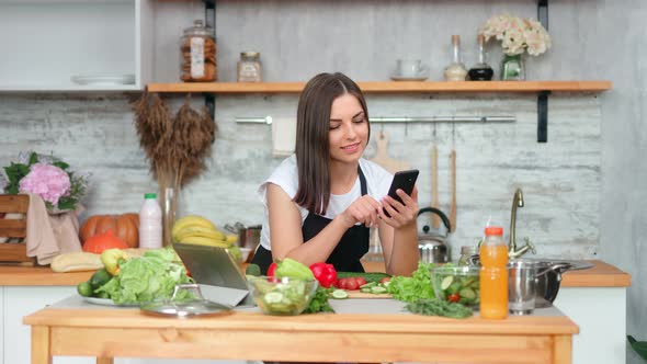 Attractive Beautiful Woman in Apron Chatting Using Smartphone Cooking Meal at Kitchen