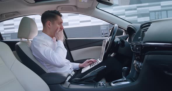 Shocked Businessman Scared By Reading Bad Email on His Laptop Computer Sitting in the Driver's Seat