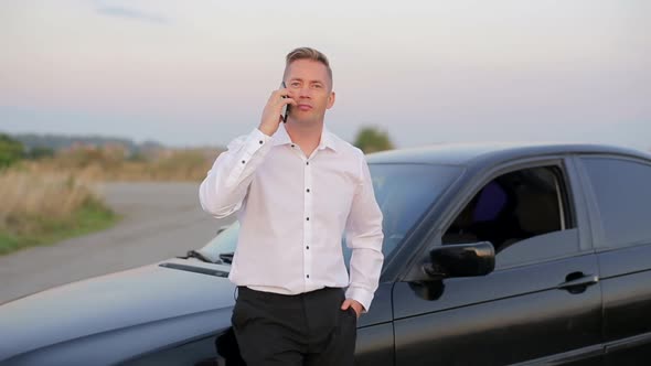 Handsome smiling businessman standing near car and using mobile phone.