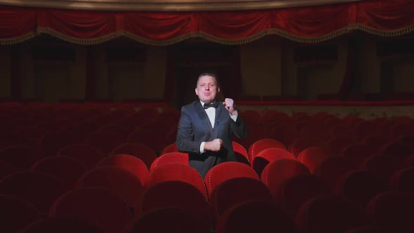 Happy man in dark empty theatre hall. Rich man in suit standing among vacant red armchairs 