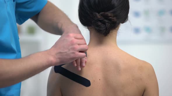 Physiotherapist Applying Y-Shaped Tapes on Female Patient Shoulder Muscle Strain