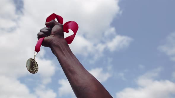 Hand of black man raises gold medal against blue sky, the concept of victory. Black man raises his h