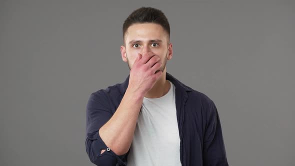 Portrait of Man in Casual Clothing Being Deeply Shaken By Bad News and Covering Open Mouth in Shock