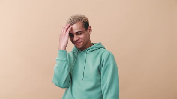 Confused positive curly-haired man wearing blue hoodie looking at the camera