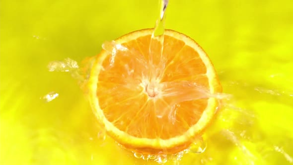 Water pours on an orange juicy orange on a yellow background slow motion. Orange slice and water