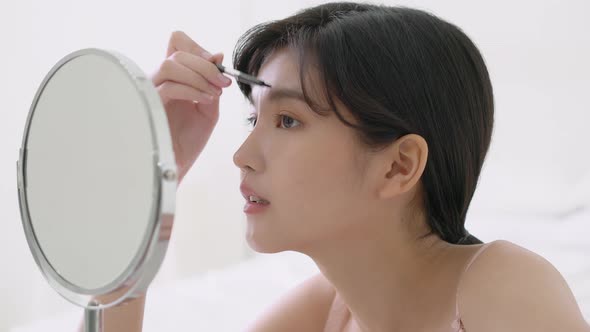 Beautiful young asian woman applying makeup eyebrows brush.