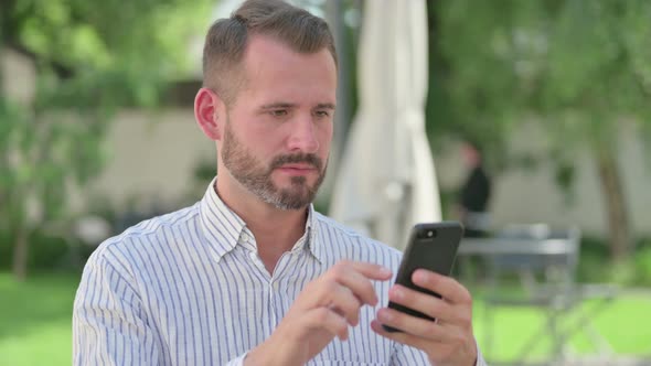 Outdoor Portrait of Middle Aged Man Reacting to Loss on Smartphone