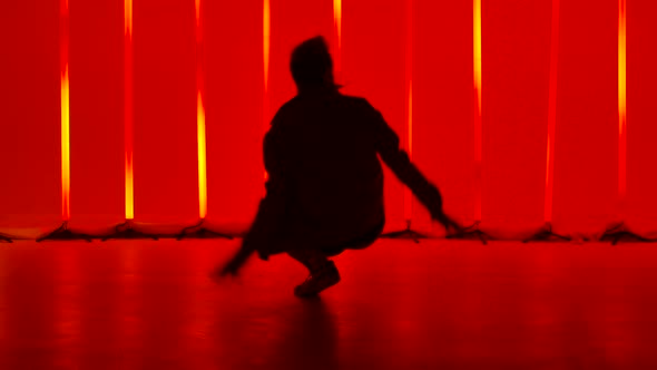 Stylish Male Break Dance Dancer Performs a Spin on the Floor in a Dark Studio Against the Backdrop