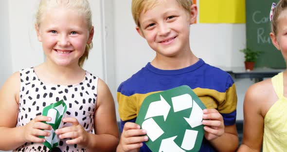 School kids holding recycling symbols and globe in classroom