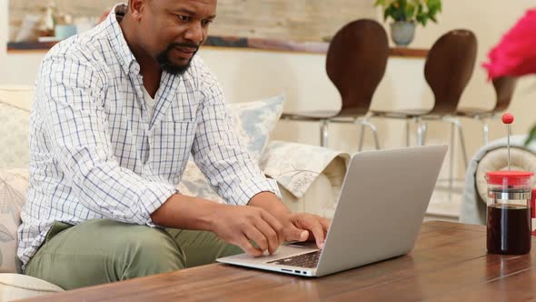 Man using laptop while having coffee in living room 