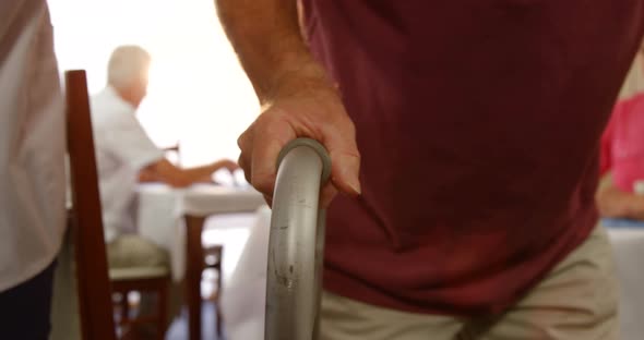 Mid section of doctor assisting a senior man to walk with walking frame