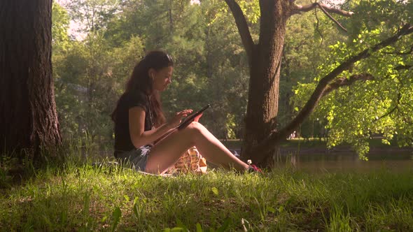 Young Woman In Park Uses Smartphone And Tablet