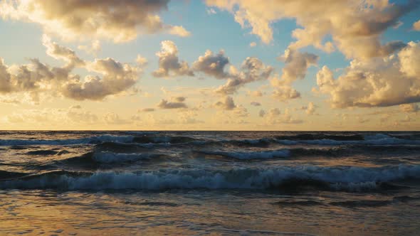 Sunset Behind Clouds Over Sea Waves and Sandy Beach