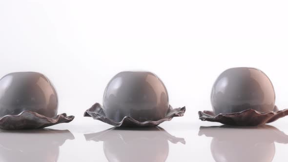 Three Desserts in the Form of Pearl with Gray Glaze Spinning on White Background