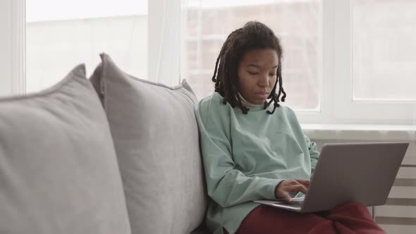 Young African Woman Sitting on Couch with Laptop