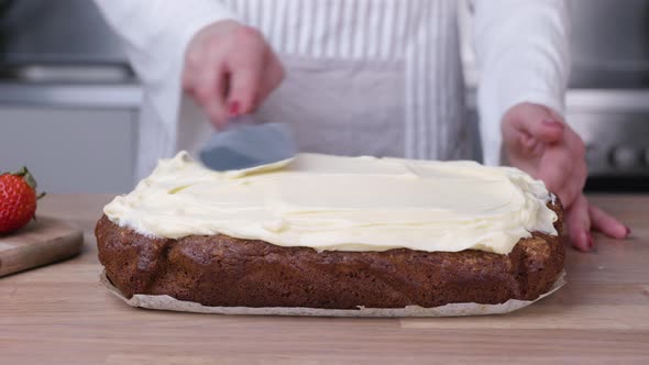 Female Baker Spreading White Frosting on Carrot Cake with Spatula. - Slider Left