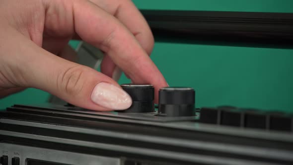 Girl's Hand Twists the Levers on Retro Radio Tape Recorder on a Green Background