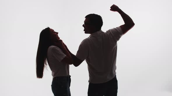 Silhouette of a family couple fighting. Man grabs woman by her neck and shakes his fist in the air