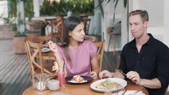 Young Man and Woman Sit in Outdoor Cafe, Eat Healthy Food and Talk