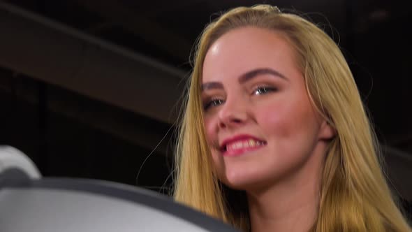 A Young Beautiful Woman Walks on a Treadmill in a Gym and Smiles at the Camera - Face Closeup