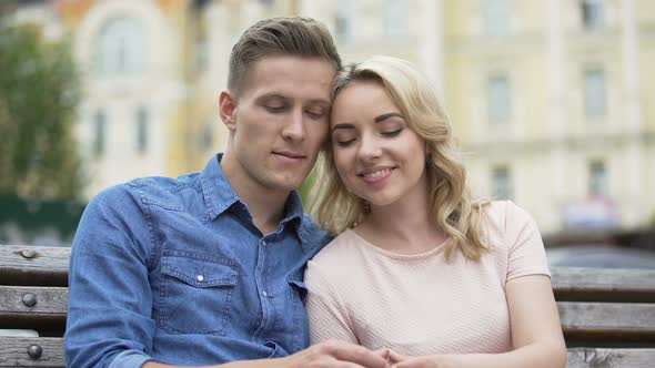 Female and male sitting close to each other, putting up finger-shaped heart