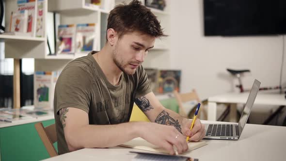 Attractive Young Male Programmer Teacher Writes Something Down in His Notebook Looking Very Serious