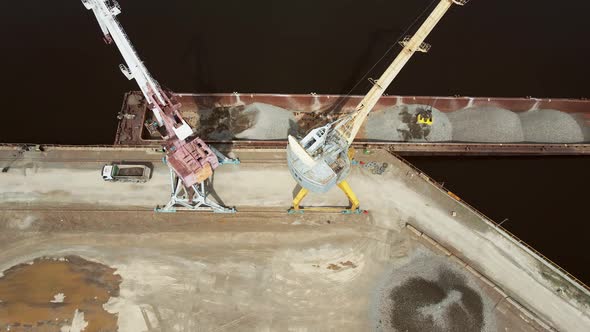 Huge Harbor Cranes on the River Bank Unload Rubble From a Barge