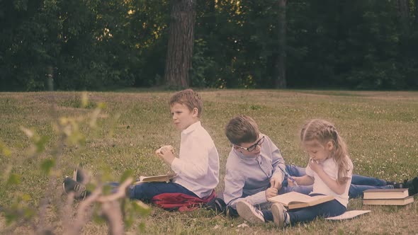 Pupils Sit on Grass Read Books and Discuss Home Assignment