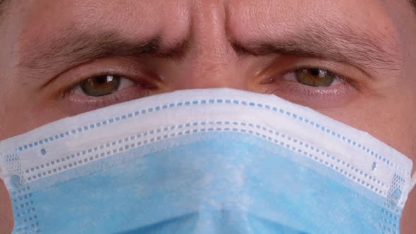 Young Man in a Medical Protective Face Mask Looking at the Camera on the Street Background