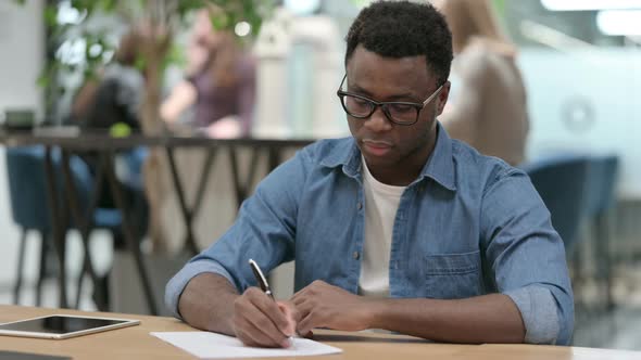 Hardworking Young African Man Writing on Paper in Modern Office