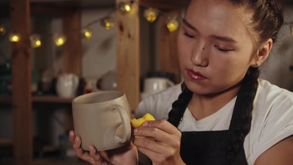 Young Asian Woman Potter Smoothing Out the Clay Cup Using a Yellow Wet Sponge