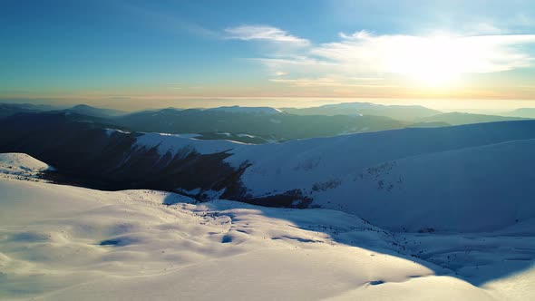 Flight over the snowy mountains illuminated by the evening sun