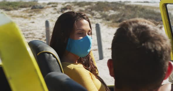 Happy caucasian couple wearing face masks sitting in beach buggy