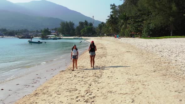 Female models happy and smiling on idyllic seashore beach voyage by blue green water and white sand 