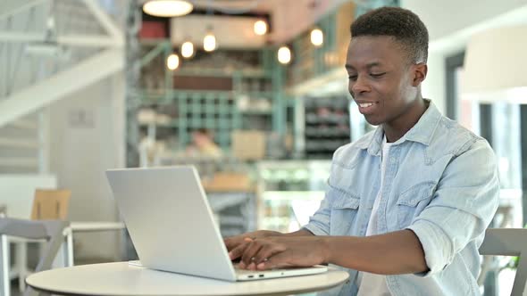 Cheerful Young African Man Working on Laptop in Cafe