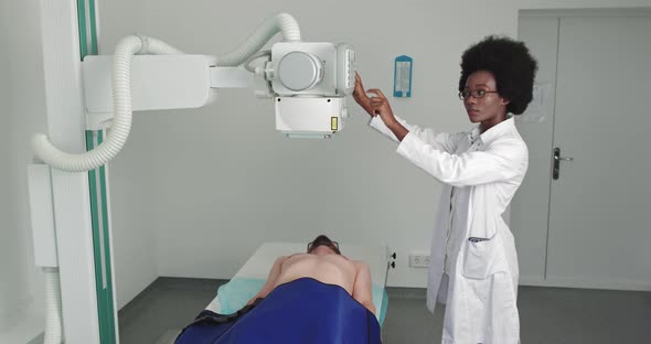 In the Hospital Man Lying on a Bed Female Technician Adjusts XRay Machine