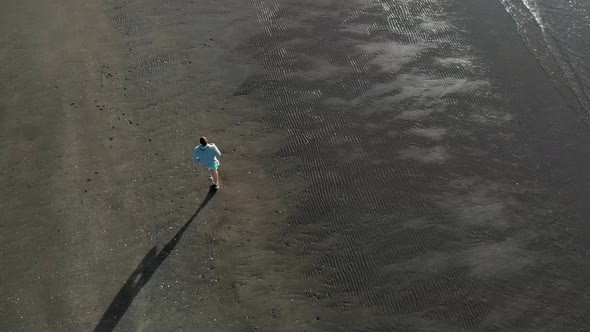 Aerial top down tracking shot of young caucasian man running on a beach in Auckland, New Zealand