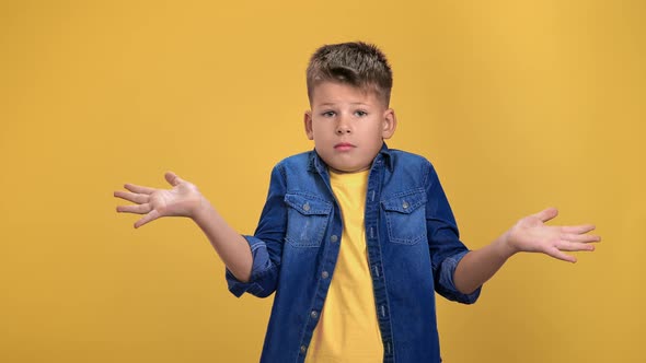 Puzzlement Cute Boy Kid Gesturing Dont Know Not Sure with Spreading Arms Posing Isolated on Orange