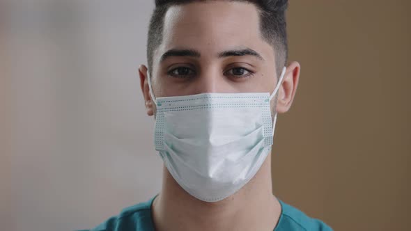 Close Up Young Hispanic Man Doctor Arabian Male Face in Medical Mask with Dark Eyes Looking at