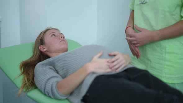 Young Focused Pregnant Woman Listening to Unrecognizable Doctor Lying on Examination Couch in