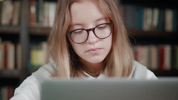 Tired Young Female Schoolkid is Working on Laptop Computer at the Desk in Cozy Room Over Library