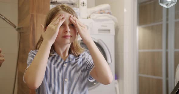 The Teenage Girl Takes Care of the Morning in the Bathroom Looking in the Mirror