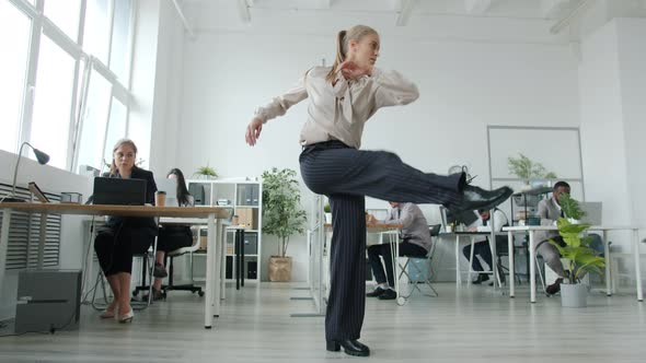 Pretty Young Woman Performing Creative Modern Dance in Workplace While Colleagues Busy with Work