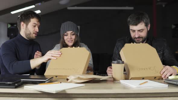 Team of Young Creative Workers Opening Paper Boxes with Pizza Being Surprised and Happy