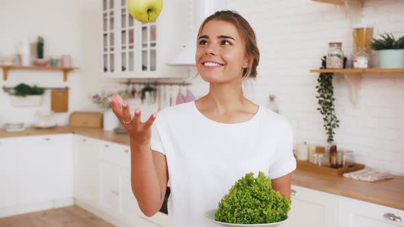 Woman is Throwing Up Apple and Eating It Holding Green Salad Leaves