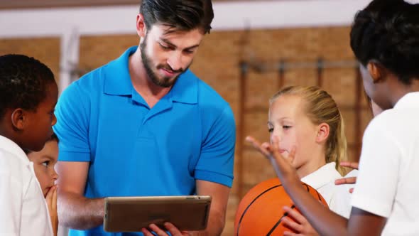 Sports teacher and school kids using digital tablet in basketball court